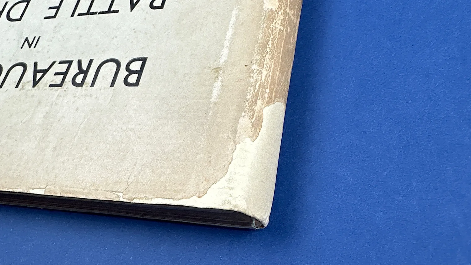 Close-up of corner wear on Bureaucrats in Battledress, showing surface paper loss to the outer cover layer