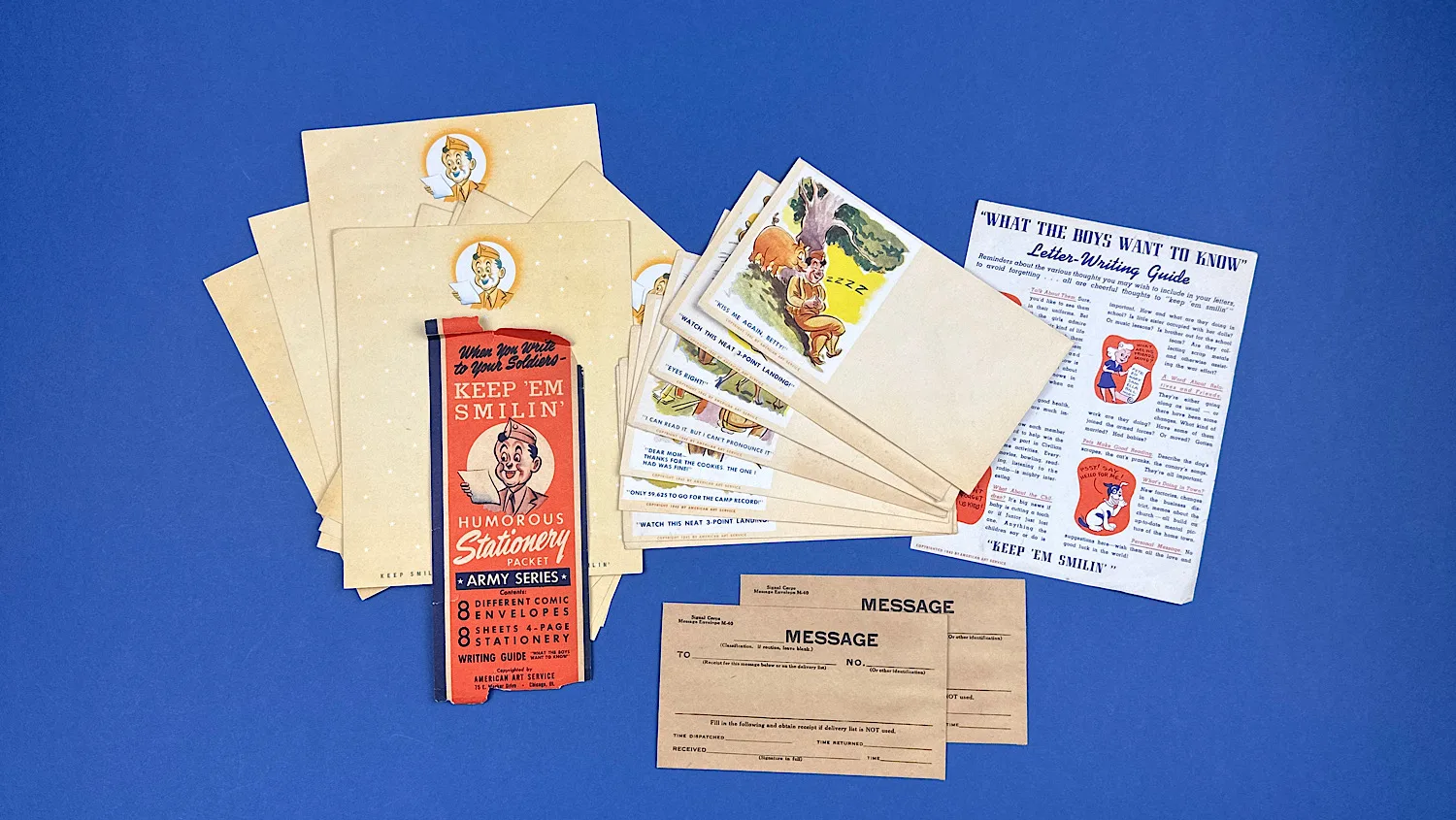 Complete WW2 US Army Keep ’Em Smilin’ humorous stationery group showing packet wrapper envelopes writing paper writing guide and Signal Corps message envelopes laid out together.