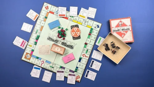 Full contents layout of pre-WW2 British Monopoly board game with board laid open showing London streets, Community Chest and Chance cards, houses, hotels, playing pieces, rule cards, money and original Waddington box arranged around the board