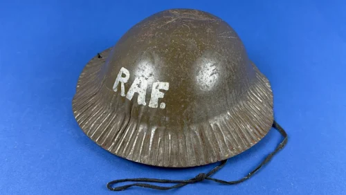 Angled front view of vintage RAF style toy helmet showing hand painted lettering and aged olive finish
