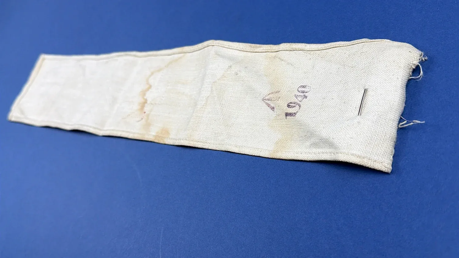 Full length reverse of WW2 British Red Cross armband showing staining and Broad Arrow with 1940 date