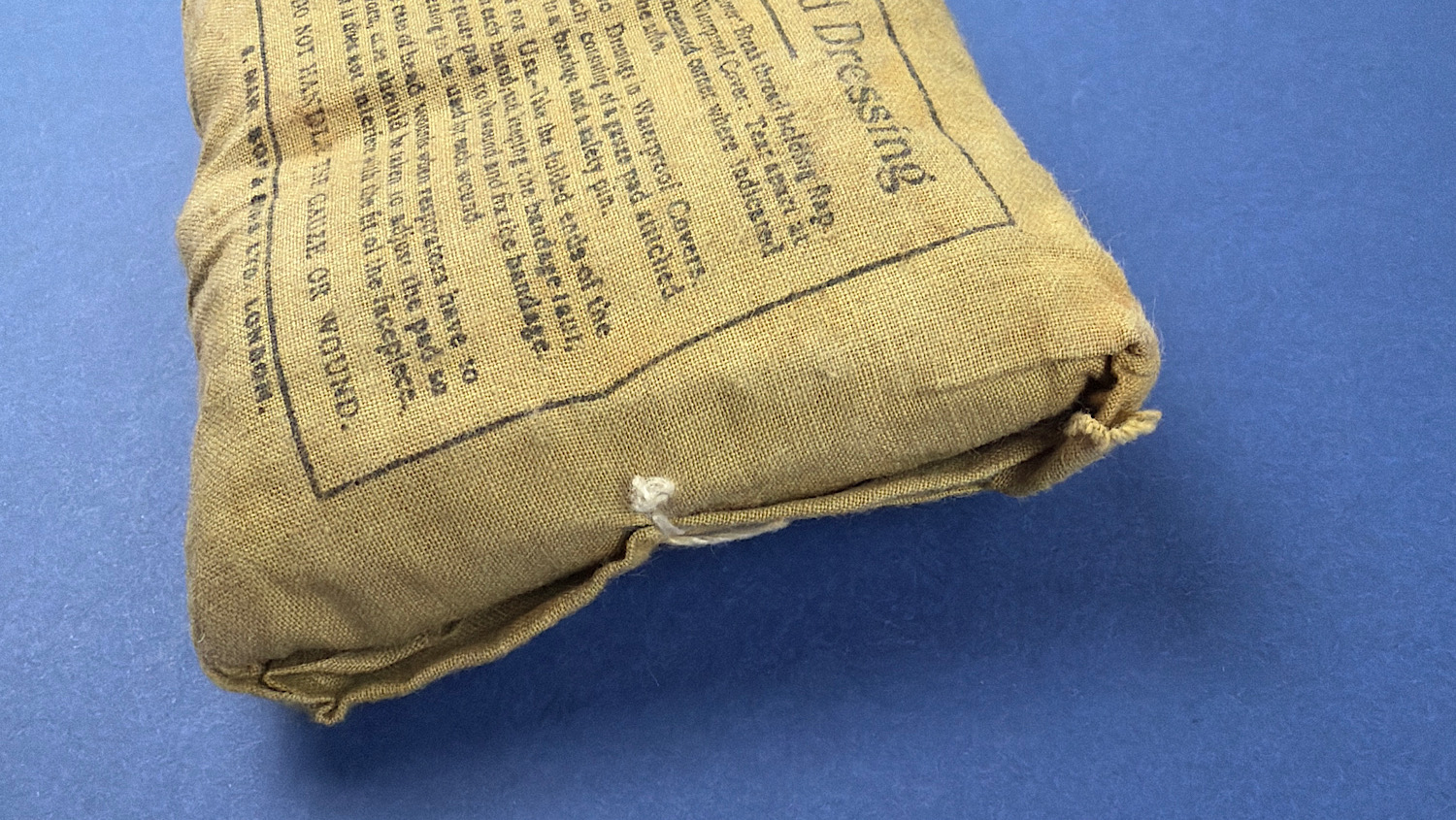 Angled view of unopened WW2 British First Field Dressing showing intact closure cord and original wrapper construction