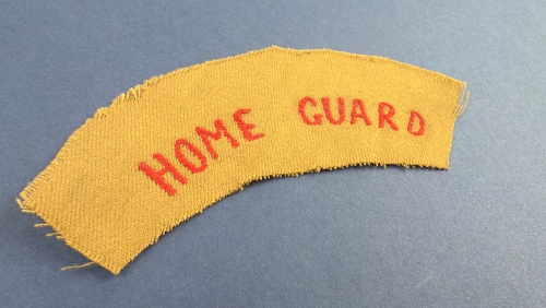 Original WW2 British Home Guard shoulder title with red embroidered lettering on khaki cloth backing