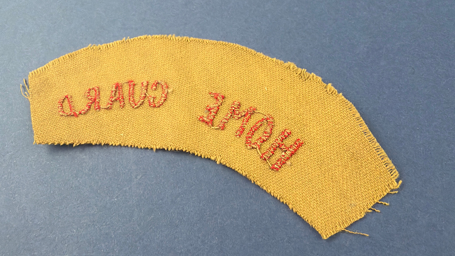 Angled reverse view of WW2 British Home Guard shoulder title with red embroidery on khaki cloth backing