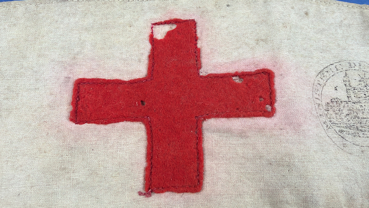 Close-up of stitched red wool Red Cross emblem showing age-related wear and small moth holes.