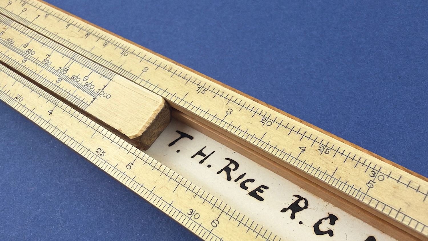 Close-up of the original WW1 Royal Garrison Artillery slide rule showing the T.H. Rice R.C. ownership inscription beneath the sliding scale.
