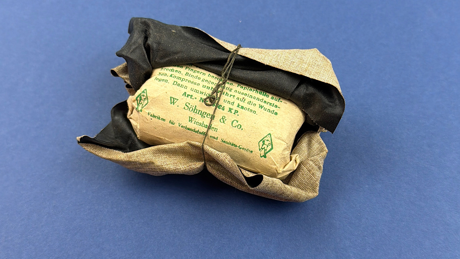 Original 1944 German WW2 Verbandpäckchen with the outer wrapper gently lifted to display the untouched black inner wrapping and original paper instructions.