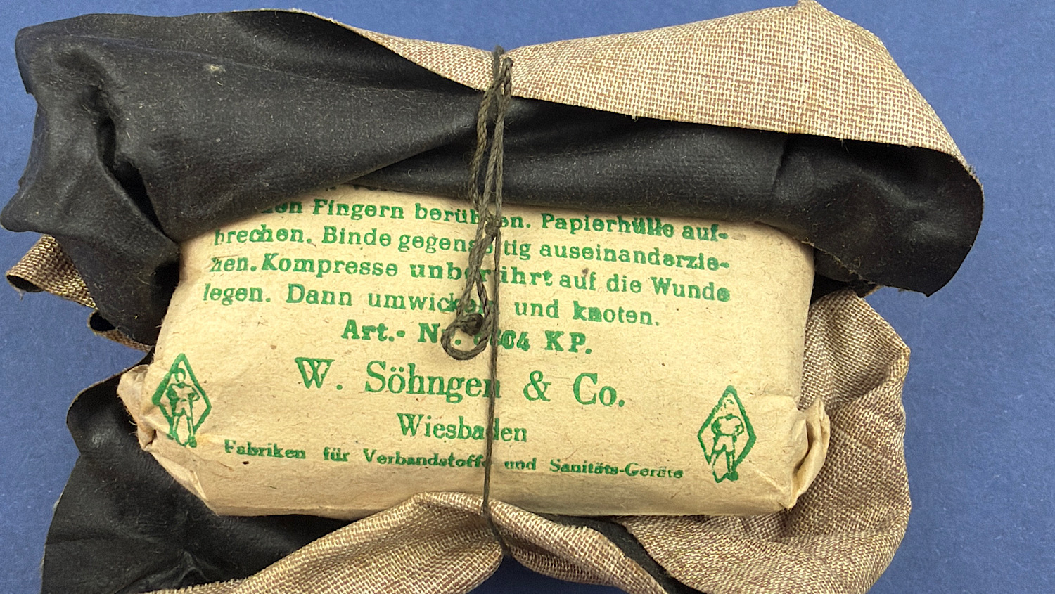 Close-up of the original paper instructions and black waterproof inner wrapper inside the unopened 1944 German WW2 Verbandpäckchen by W. Söhngen & Co.